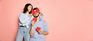 Casal brinca com corações vermelhos em um fundo rosa